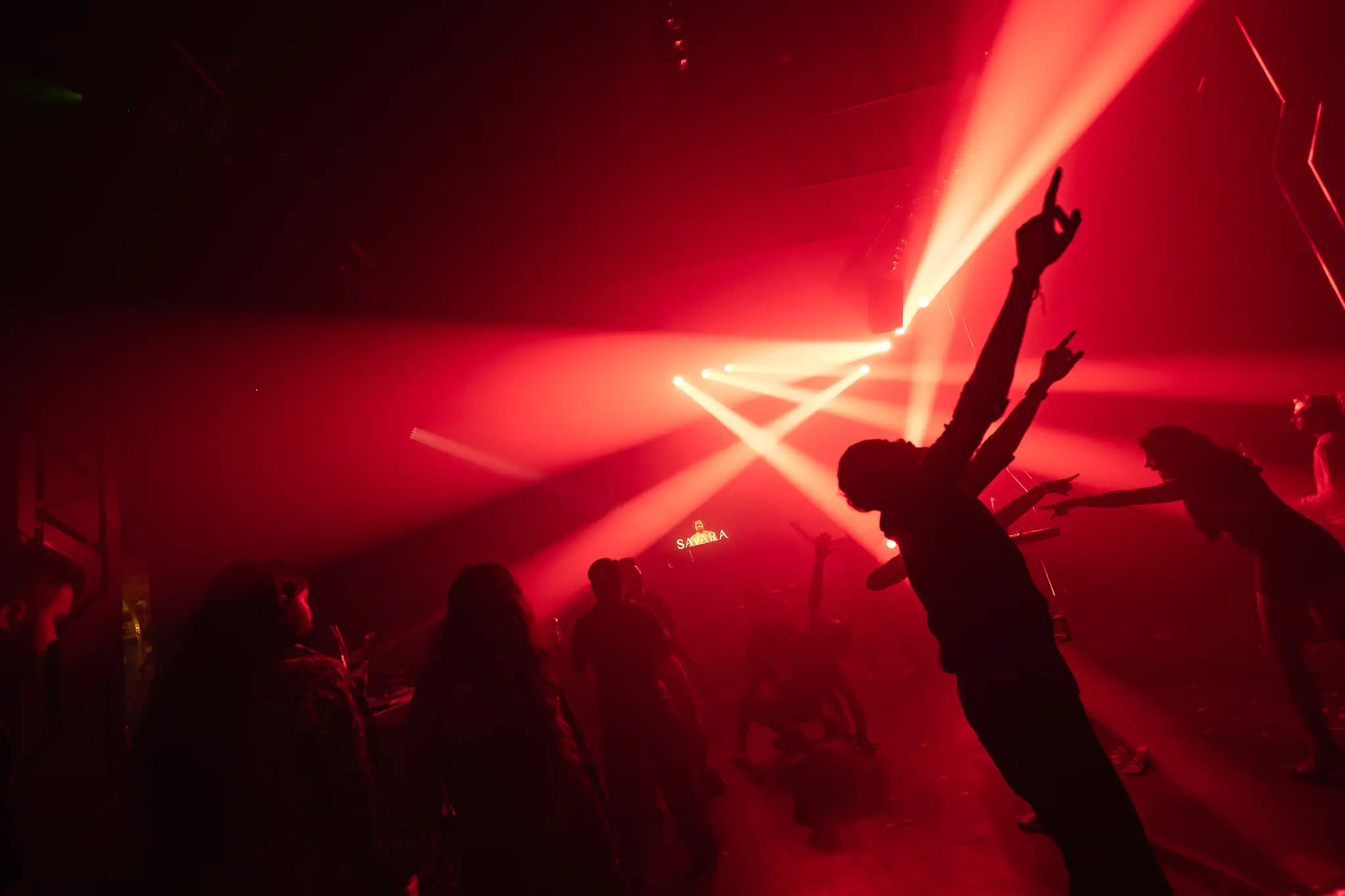 Crowd silhouetted with hands raised under red laser beams